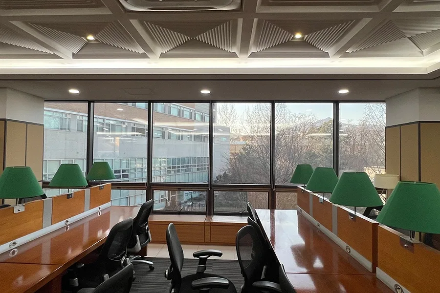 초록색 스탠드 조명이 늘어선 열람실, 통유리 창 너머로 산이 보이는 전경
