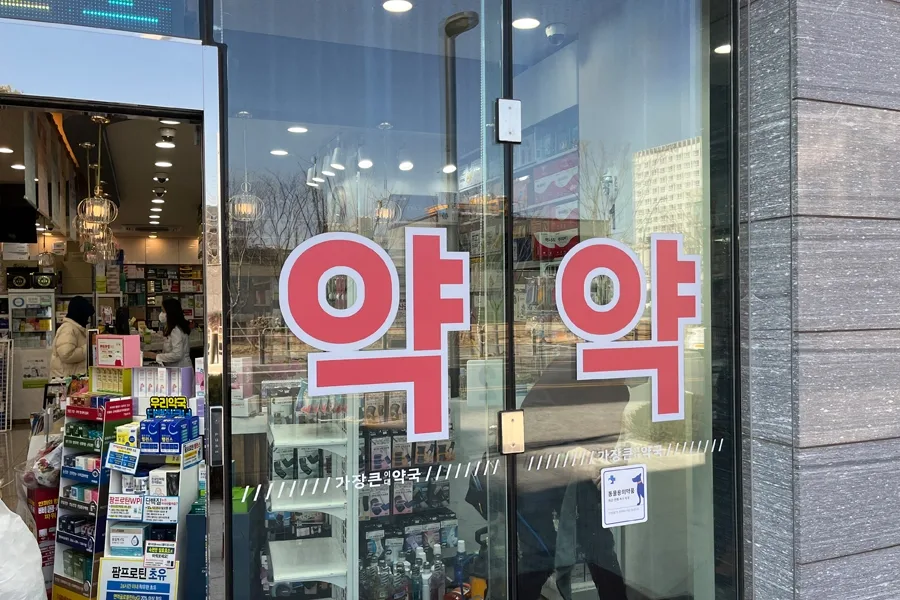 약국 출입문 안쪽에서 바라본 통유리 전경, 도트 패턴 단열필름과 약 로고 스티커가 함께 보이는 모습