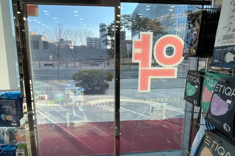 약국 출입문 유리 안쪽에서 도로 방향을 바라본 시공 후 모습, 필름을 통해 바깥 풍경이 선명하게 보이는 모습