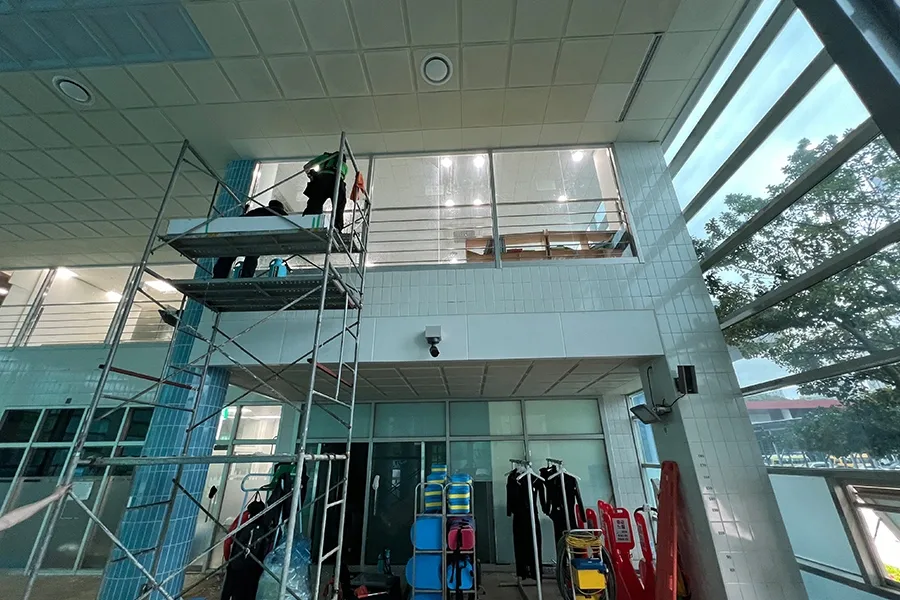 체육센터 2층 규모의 대형 유리창 전경과 비계 작업 현장, 하단에 운동 장비가 놓여 있는 모습