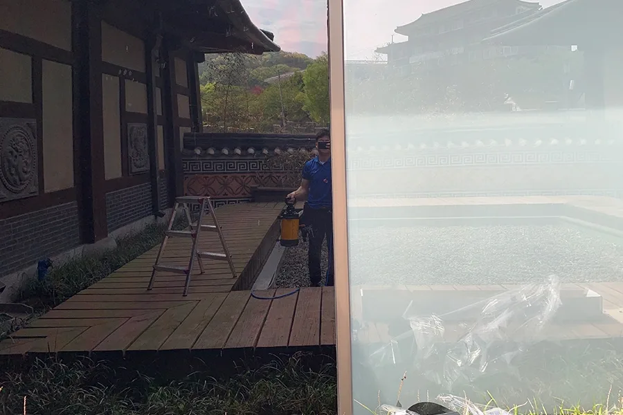 작업자가 분무기로 용액을 뿌리며 통유리에 필름을 시공하는 모습, 좌측은 필름 적용 완료 구간