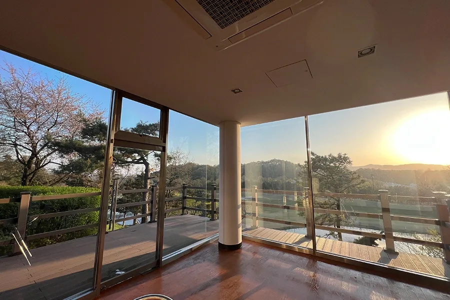 노을 지는 저녁, 통유리 너머로 산과 나무가 비치는 휴게 공간 전경