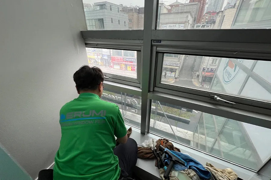 시공기사가 창틀에 걸터앉아 필름 시공 작업을 하는 모습